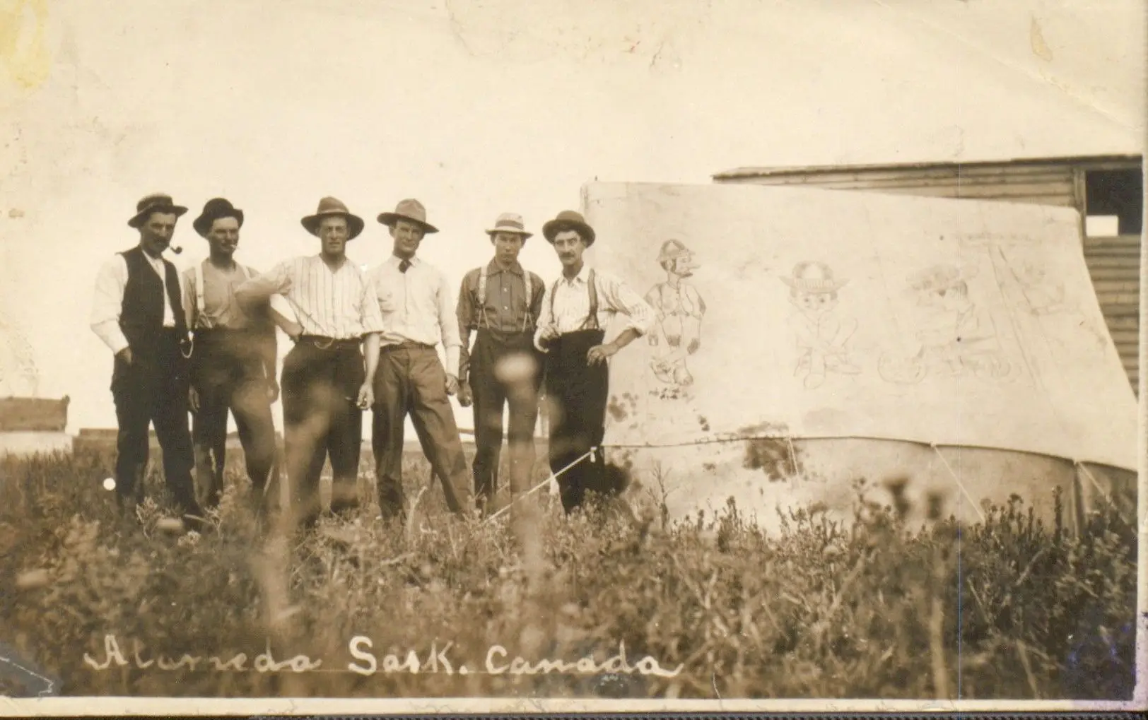 Six men standing beside a tent with cartoon drawings