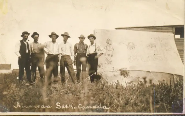 Six men standing beside a tent with cartoon drawings